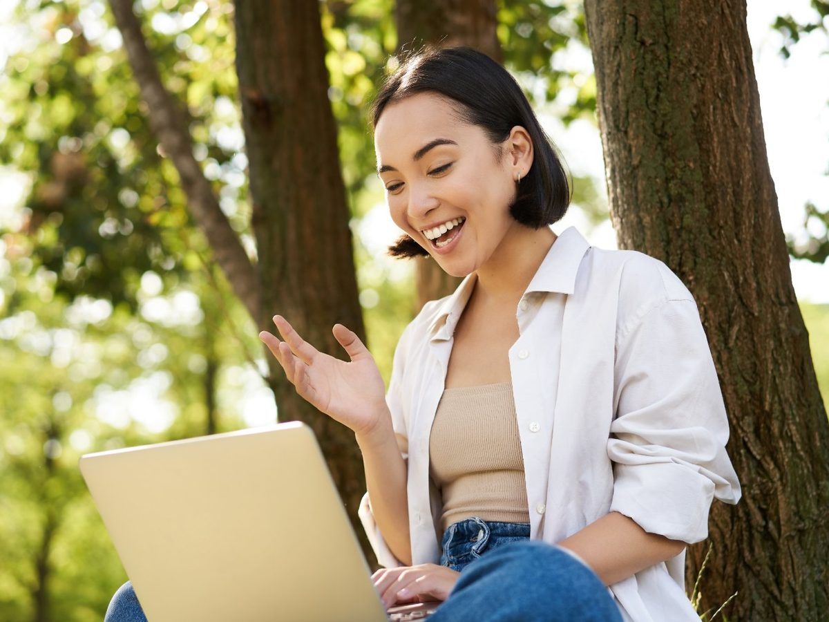 A smiling woman working on a laptop outdoors