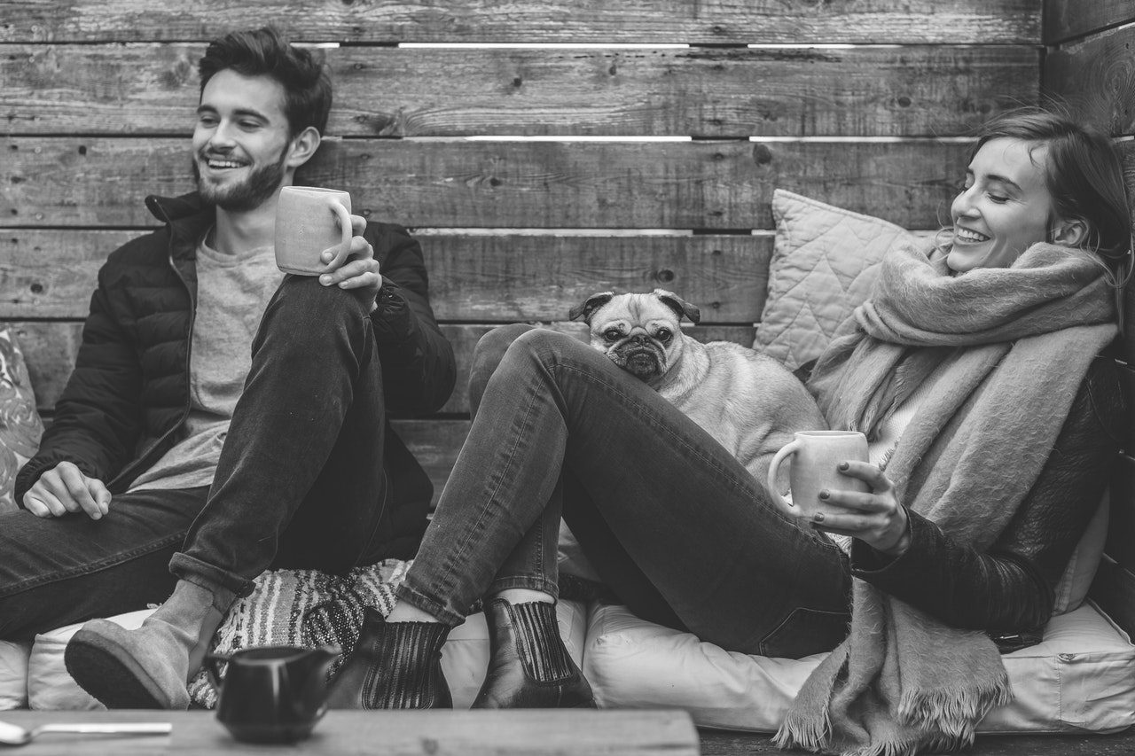 Two people laughing over coffee with a pug between them